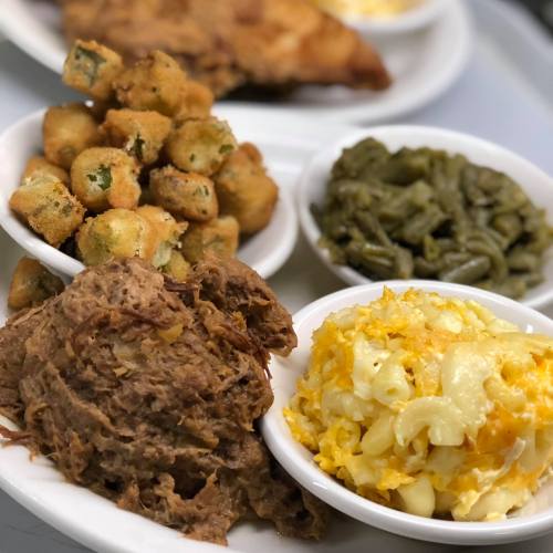 A plate featuring pulled pork, fried okra, macaroni and cheese, and green beans in small bowls.