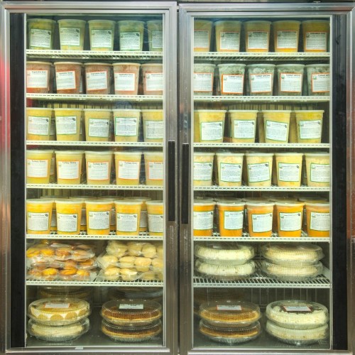 A refrigerated display case filled with various containers of desserts and pies, neatly organized on shelves.
