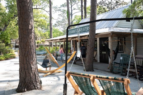 A cozy outdoor space with hammocks, a shop sign, and people enjoying the serene environment among trees.
