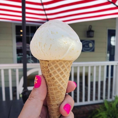 A hand holding a cone of vanilla ice cream with a red and white striped awning in the background.