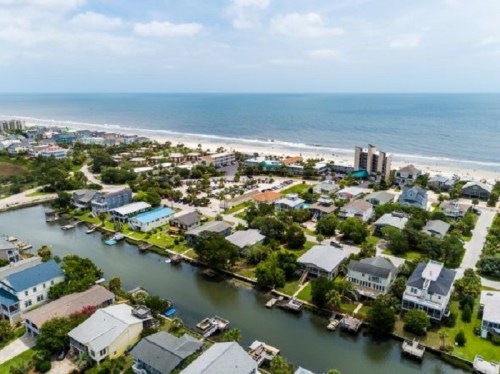 Aerial view of a coastal town with houses, canals, and a beach in the background under a clear blue sky.