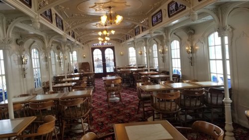 A spacious, elegantly decorated dining room with wooden tables, chairs, and large windows letting in natural light.