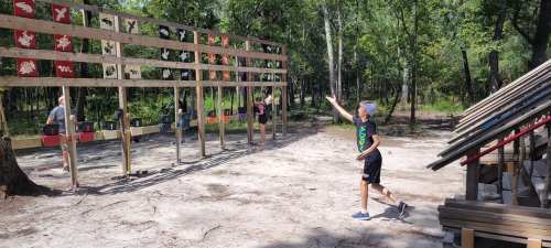 A child throws a disc towards a target in a wooded outdoor setting, with others participating in the background.