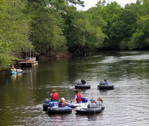 A group of people in inflatable rafts enjoying a calm river surrounded by lush greenery.
