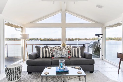 Cozy living room with a gray sofa, decorative pillows, and large windows overlooking a serene lake view.