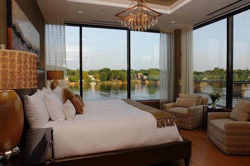 Luxurious hotel room with a king bed, elegant decor, and large windows overlooking a serene river view.