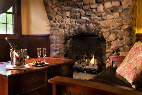 Cozy room with a stone fireplace, a wooden table with champagne and glasses, and a comfortable chair.
