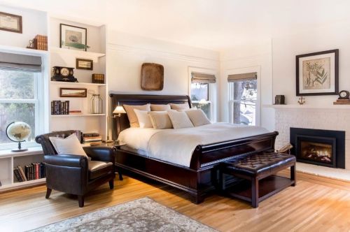 Cozy bedroom featuring a wooden sleigh bed, armchair, bookshelf, and a fireplace, with warm lighting and neutral decor.
