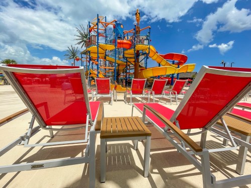 Red lounge chairs in the foreground with a colorful water slide and blue sky in the background.