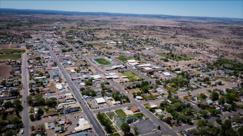 Aerial view of a small town surrounded by hills, featuring roads, buildings, and green spaces.