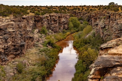 A scenic view of a canyon with a winding river surrounded by rocky cliffs and lush greenery.