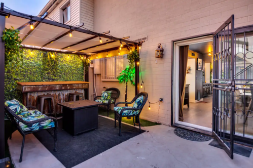 Cozy outdoor patio with a bar, string lights, and seating, leading to an interior space.