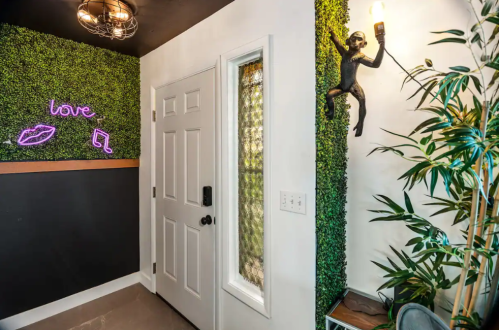 A stylish entryway with green wall decor, a neon "love" sign, and a monkey light fixture.