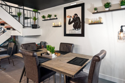 A modern dining area with wooden tables, leather chairs, and a monkey artwork on the wall, featuring plants and candles.