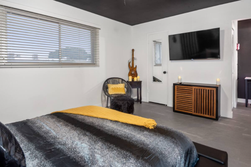Modern bedroom featuring a black bed, yellow accents, a TV, and stylish decor with a guitar and candles.