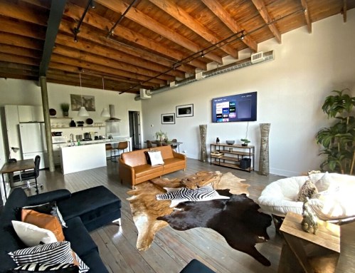 Spacious living area with wooden beams, modern furniture, a large TV, and a cowhide rug. Bright and inviting atmosphere.