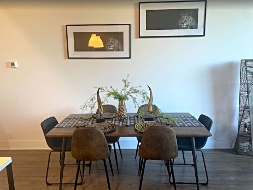 A modern dining area with a wooden table, four chairs, decorative plants, and framed artwork on the wall.