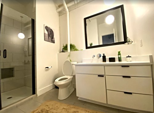 Modern bathroom featuring a shower, toilet, large mirror, and sleek vanity with storage. Light and airy design.
