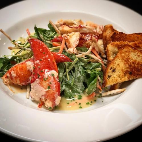 A fresh salad with lobster, mixed greens, and toasted bread, drizzled with a light dressing.