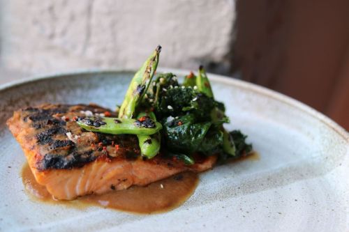 Grilled salmon fillet topped with sautéed greens and green beans on a rustic plate.