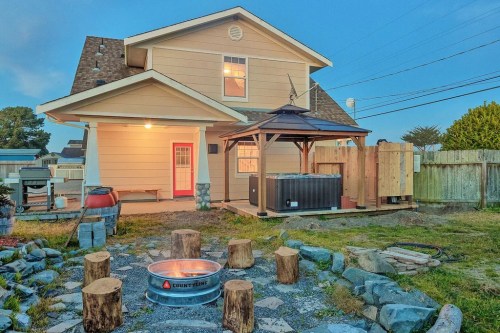 A cozy backyard with a fire pit, seating logs, a hot tub, and a gazebo near a charming house at dusk.