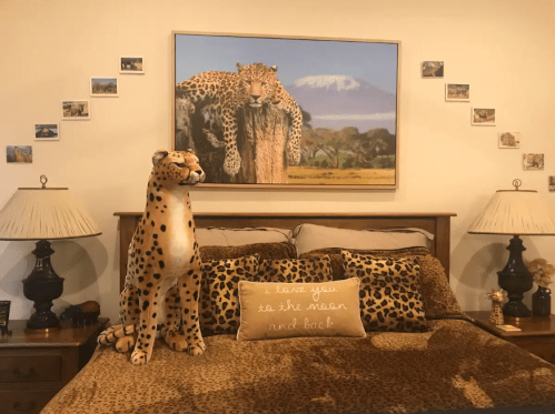 A cozy bedroom with leopard print decor, featuring a stuffed leopard and a mountain landscape painting.