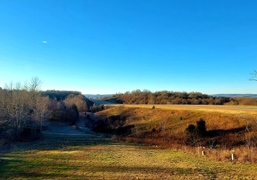 A scenic landscape featuring rolling hills, bare trees, and a clear blue sky, with fields stretching into the distance.