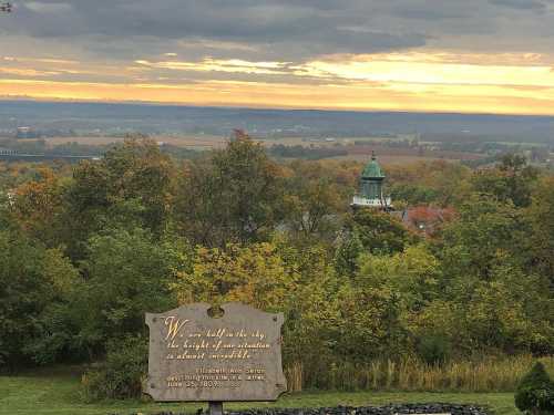 A scenic view of rolling hills and a cloudy sky, with a historical sign in the foreground.