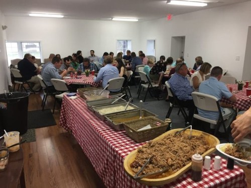 A crowded dining room with people enjoying a meal at tables covered in red and white checkered tablecloths.