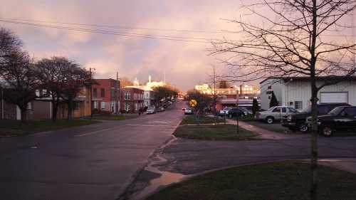 A quiet street scene at dusk, with buildings lining the road and a hint of sunset in the background.