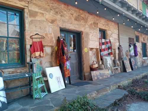 A stone building entrance with art displays, colorful clothing, and string lights hanging above.