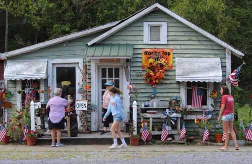 A quaint, colorful shop with a sign reading "Open," decorated with flowers and flags, as people walk by.