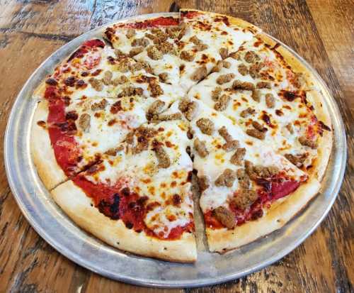 A round pizza topped with melted cheese and small pieces of sausage, sliced into eight pieces on a metal tray.