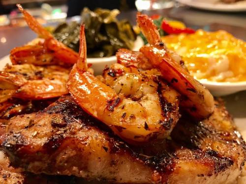 Grilled shrimp atop a juicy steak, served with collard greens and a side of cheesy rice.