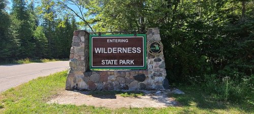 Sign marking the entrance to Wilderness State Park, surrounded by trees and greenery.