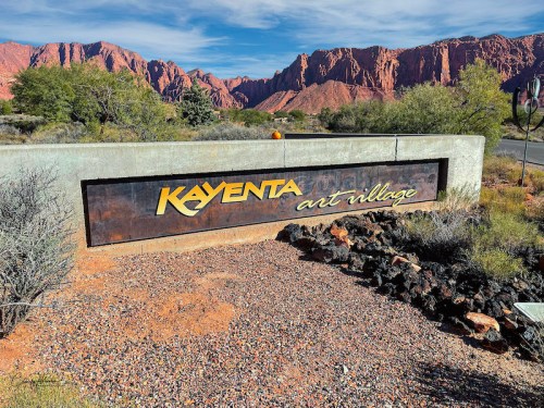 Sign for Kayenta Art Village, surrounded by desert landscape and red rock formations under a clear blue sky.