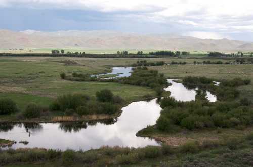 A winding river flows through a lush green landscape under a cloudy sky, surrounded by rolling hills.