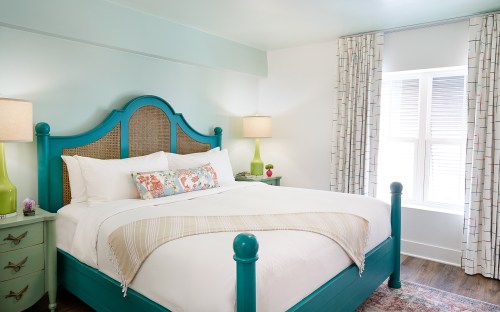 Bright bedroom featuring a turquoise bed, light curtains, and soft lighting, creating a cozy and inviting atmosphere.