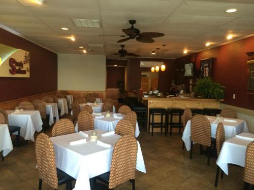 A spacious restaurant interior with white tablecloths, wicker chairs, and a bar area, featuring warm lighting and decor.