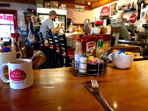A cozy diner scene with a wooden counter, coffee mugs, condiments, and patrons enjoying their meals in the background.