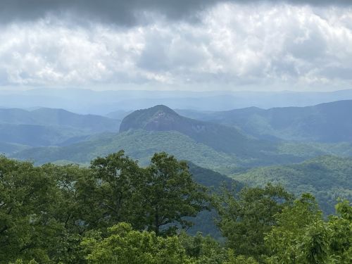 A scenic view of rolling green mountains under a cloudy sky, featuring a prominent peak in the distance.