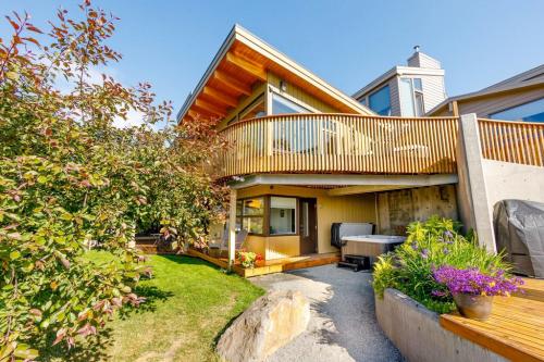 Modern house with a wooden deck, surrounded by greenery and flowers, featuring a stone pathway and outdoor seating.