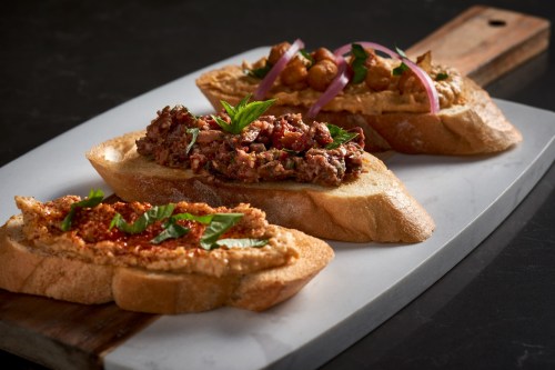 Three slices of toasted bread topped with various spreads, garnished with herbs and onions, on a white serving platter.