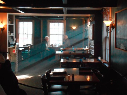 A cozy restaurant interior with sunlight streaming through windows, two patrons seated at a table.
