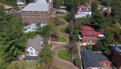 Aerial view of a winding path through greenery, surrounded by various buildings and homes in a residential area.