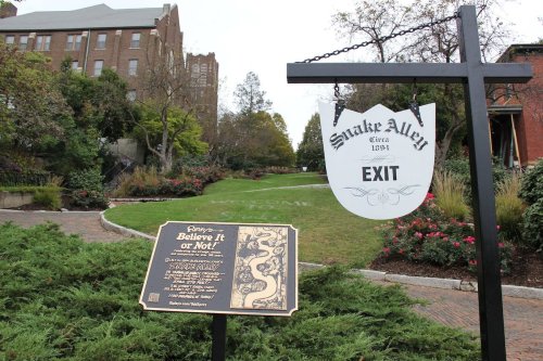 Sign for Snake Alley with an exit marker, surrounded by greenery and buildings in the background.