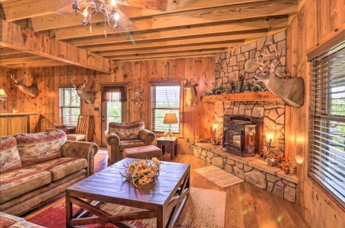 Cozy rustic living room with wooden beams, stone fireplace, and deer mounts on the walls, featuring comfortable seating.