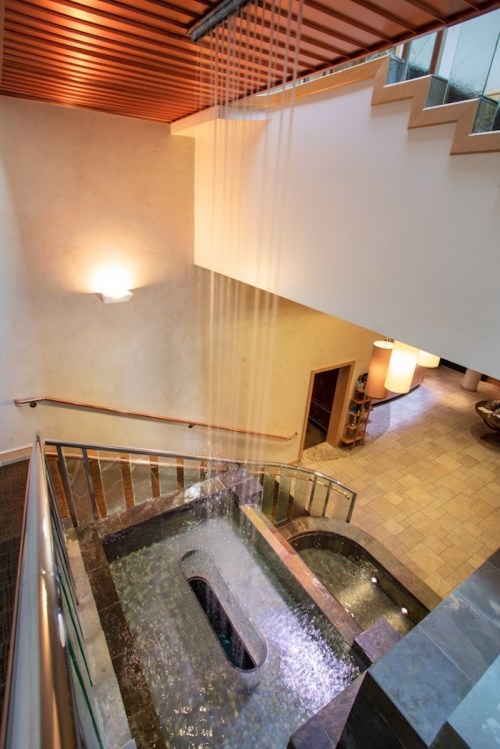 A serene indoor space featuring a water feature, stairs, and soft lighting, creating a calming atmosphere.