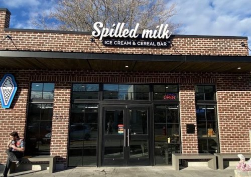 Exterior of "Spilled Milk" ice cream and cereal bar, featuring a brick facade and large windows, with an open sign.