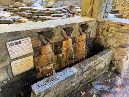 A stone spring with water flowing over a brick structure, surrounded by natural scenery and a sign labeled "Spring #2."